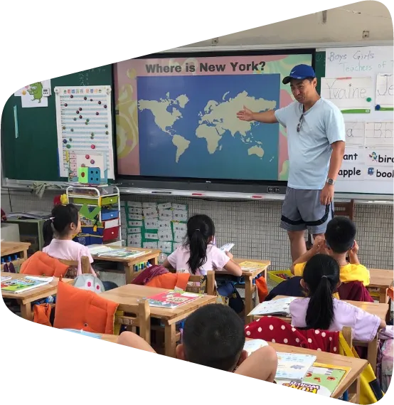 a man standing in front of a classroom full of children showing them where New York is on a map